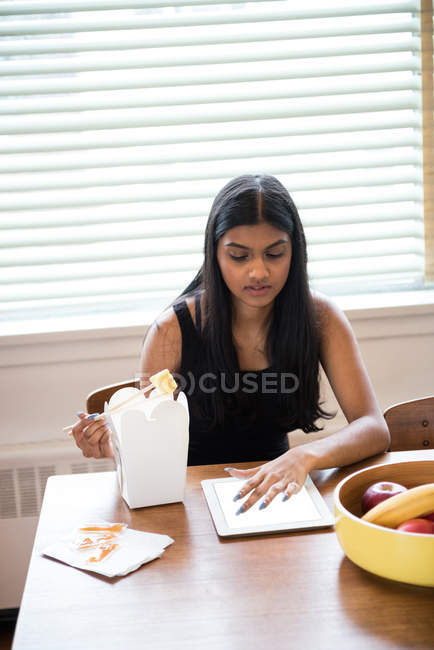 Mulher usando tablet digital enquanto almoça em casa — Fotografia de Stock