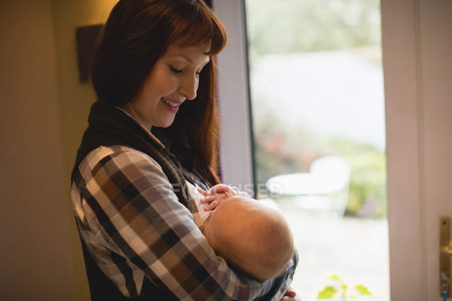 Cheerful mother breastfeeding baby at home window — Stock Photo