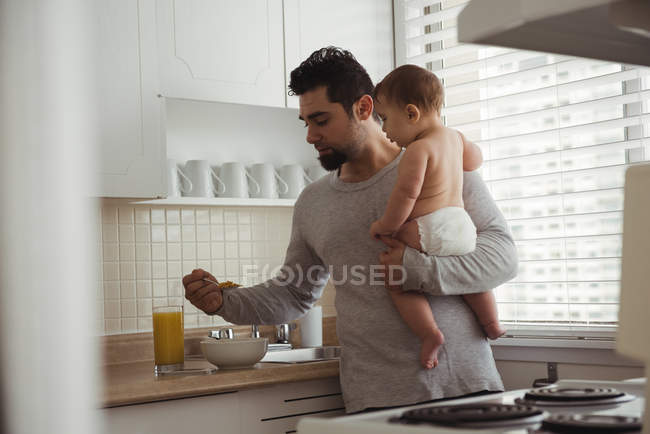 Отец завтракает, держа мальчика на кухне — стоковое фото