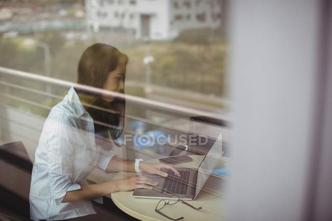 Businesswoman working on laptop in office behind glass — Stock Photo