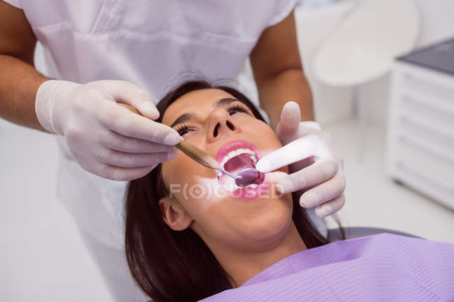 Крупный план стоматолога, осматривающего зубы пациента с зеркалом во рту — стоковое фото