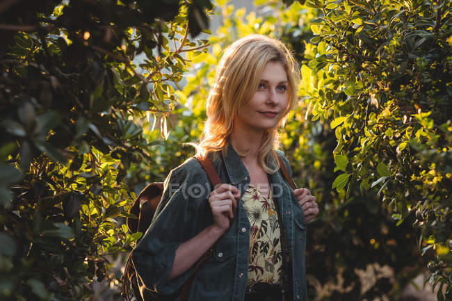 Задумчивая женщина, стоящая с сумкой в лесу — стоковое фото