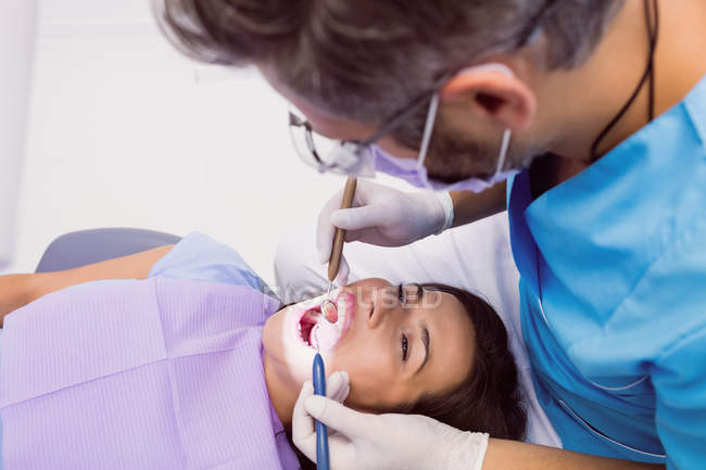 Dentista examinando paciente femenina con herramientas en clínica dental - foto de stock