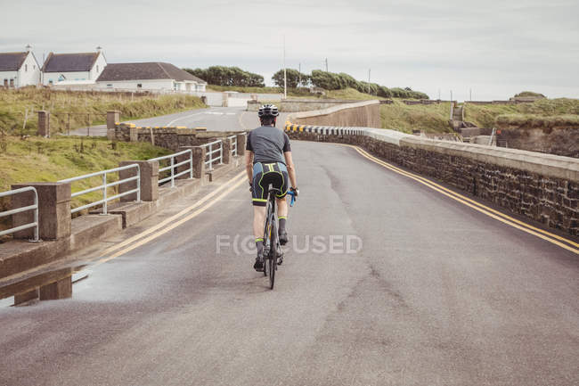 Rear view of athlete riding bicycle on country road — Stock Photo