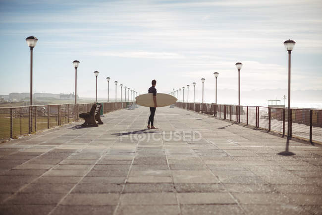 Surfista caminhando com prancha no cais na praia — Fotografia de Stock