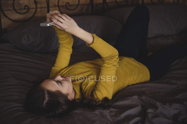 Mulher deitada na cama usando telefone celular no quarto em casa — Fotografia de Stock