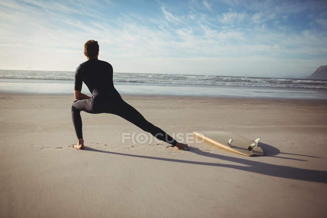 Vista trasera del hombre con tabla de surf haciendo ejercicio en la playa - foto de stock