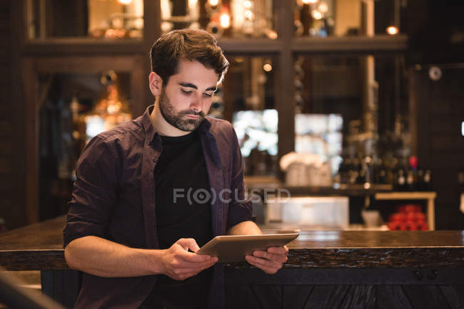 Hombre guapo sentado en el mostrador de bar y el uso de tableta digital - foto de stock
