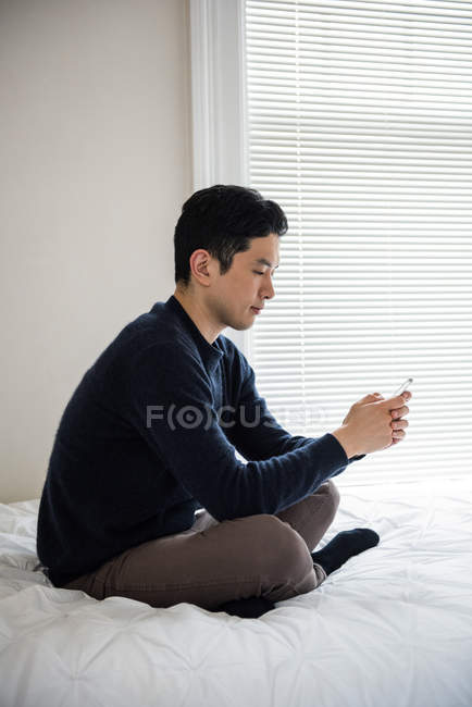 Uomo che utilizza il telefono cellulare sul letto a casa — Foto stock