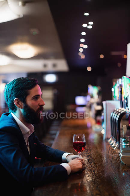 Улыбающийся бизнесмен пьет бокал вина на прилавке в баре — стоковое фото