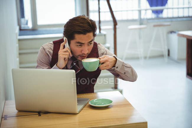 Homme parlant sur un téléphone portable tout en prenant un café dans un café — Photo de stock