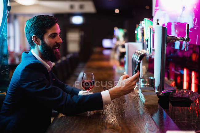 Businessman using mobile phone with glass of red wine at bar — Stock Photo