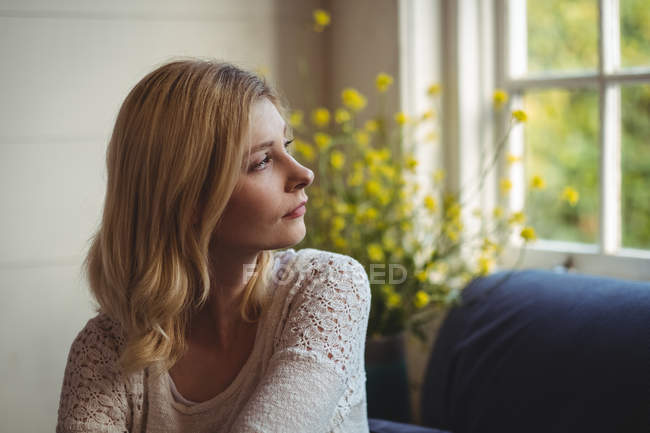 Beautiful woman looking through window in living room at home — Stock Photo