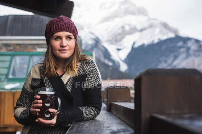 Женщина в зимней одежде держит бокал пива на открытой террасе — стоковое фото