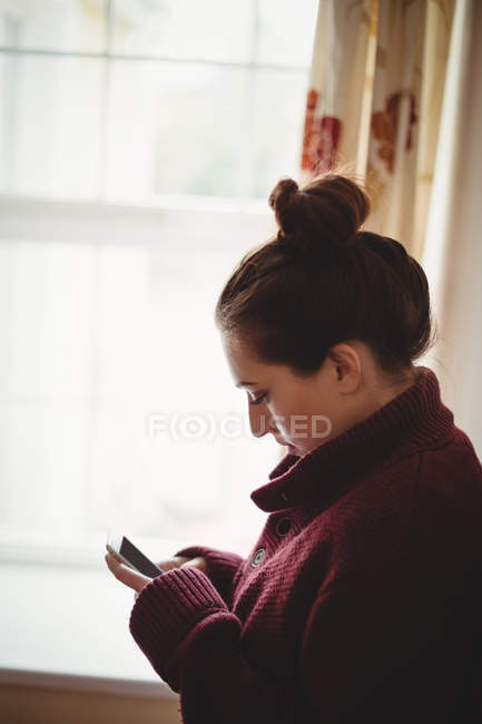Mulher usando telefone celular perto da janela em casa — Fotografia de Stock