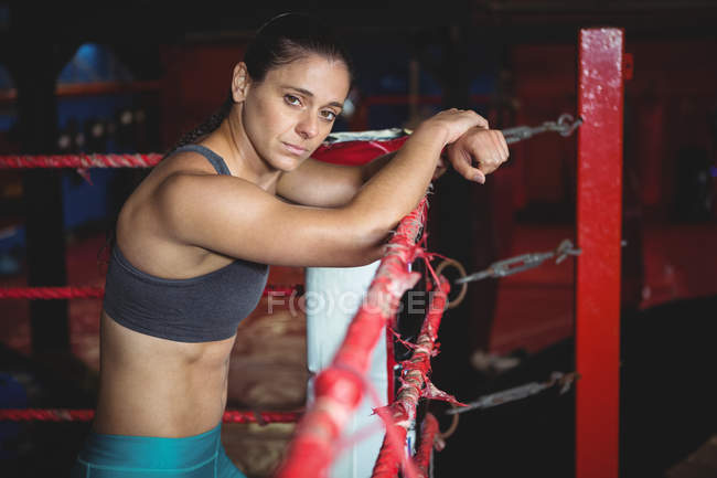 Boxeadora femenina segura apoyada en el ring de boxeo en el gimnasio - foto de stock