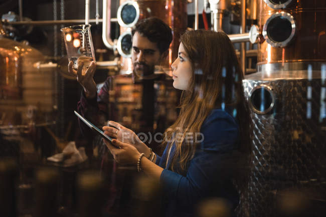 Homme et femme examinant un échantillon d'alcool dans une usine de bière — Photo de stock