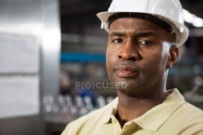 Primer plano del retrato empleado masculino serio que usa sombrero duro en fábrica - foto de stock
