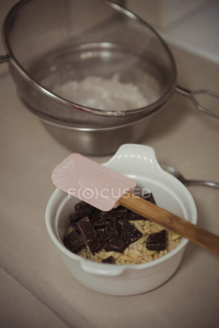 Close-up of bowl with chocolate, almonds pieces and spatula in kitchen — Stock Photo