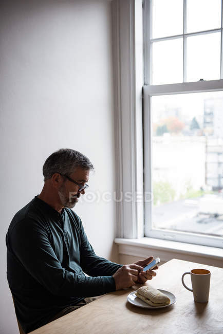 Мужчина сидит за столом и пользуется мобильным телефоном дома — стоковое фото