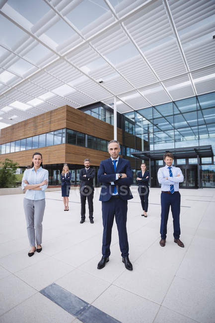Groupe d'hommes d'affaires confiants debout les bras croisés devant un immeuble de bureaux — Photo de stock
