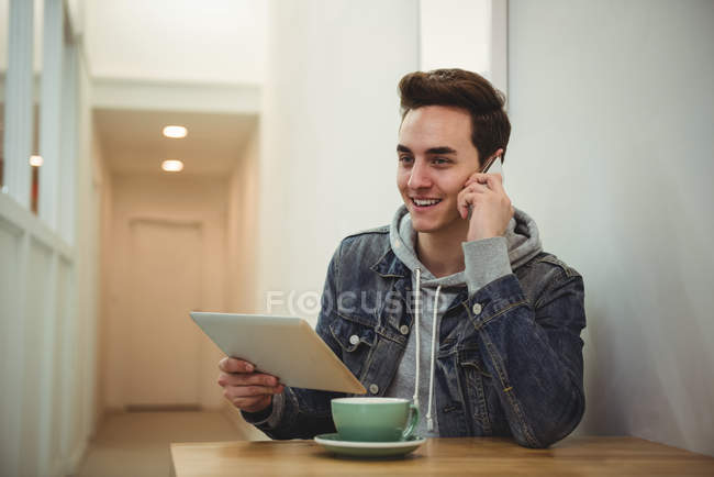 Mann telefoniert mit Handy, während er digitales Tablet im Café hält — Stockfoto