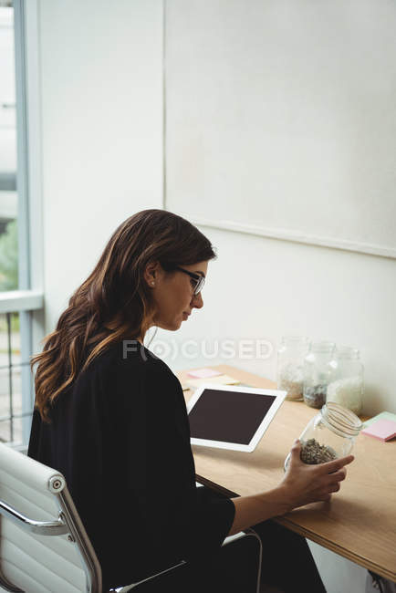 Business executive looking at jar of pebbles in office — Stock Photo