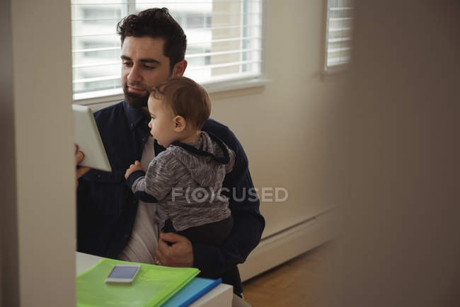 Отец держит своего ребенка во время использования цифровой планшет на столе в домашних условиях — стоковое фото