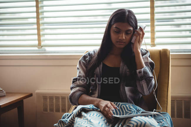 Femme écoutant de la musique avec écouteurs et tablette numérique dans le salon à la maison — Photo de stock