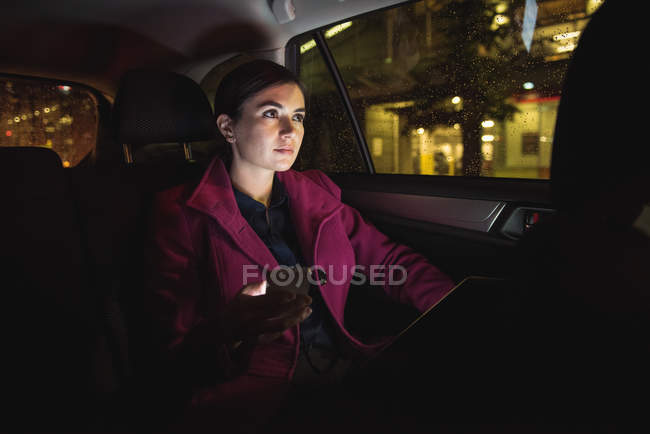 Femme d'affaires réfléchie avec tablette numérique et téléphone dans la voiture — Photo de stock