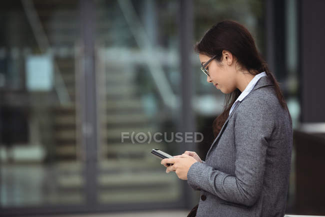 Бізнес-леді смс на мобільному телефоні, стоячи на міській вулиці — стокове фото