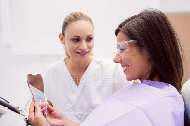 Paciente femenina sonriendo mientras se mira en el espejo en la clínica - foto de stock