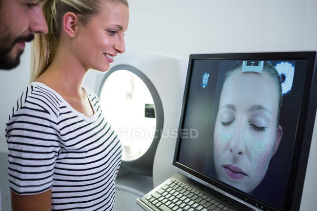 Mujer buscando informe de escaneo de resonancia magnética en la pantalla del ordenador en la clínica - foto de stock