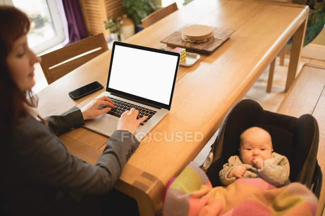 Mother using laptop while taking care of baby at home — Stock Photo