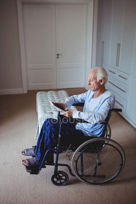 Старший мужчина сидит на инвалидной коляске и использует цифровой планшет дома — стоковое фото