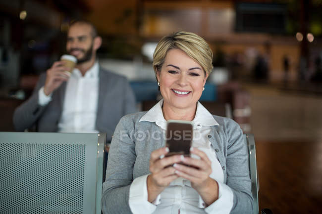 Lächelnde Geschäftsfrau mit Handy im Wartebereich am Flughafen-Terminal — Stockfoto