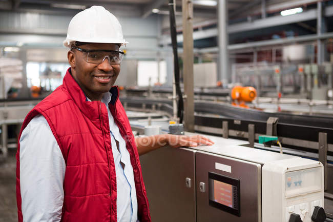 Retrato del empleado masculino sonriente de pie junto a la máquina en la fábrica de zumos - foto de stock