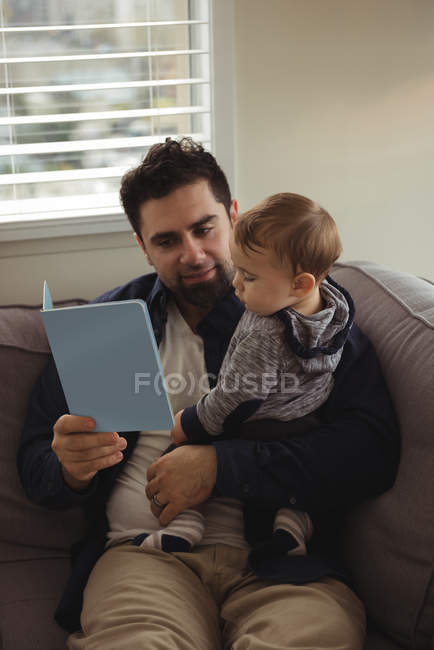 Батько читає книгу, тримаючи дитину вдома — стокове фото
