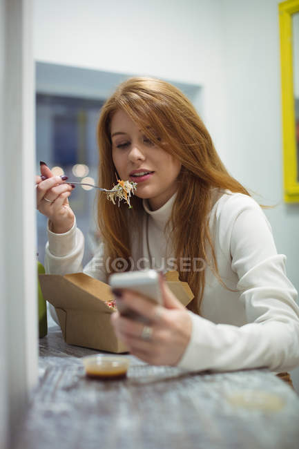 Mulher bonita usando telefone celular enquanto come salada no café — Fotografia de Stock
