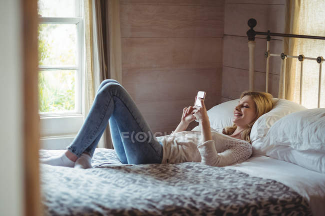 Schöne Frau auf dem Bett liegend und mit Handy im Schlafzimmer zu Hause — Stockfoto