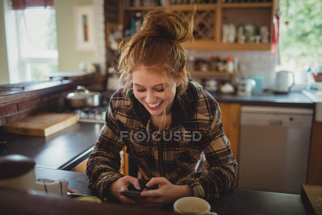Усміхнена жінка використовує мобільний телефон на кухні вдома — стокове фото