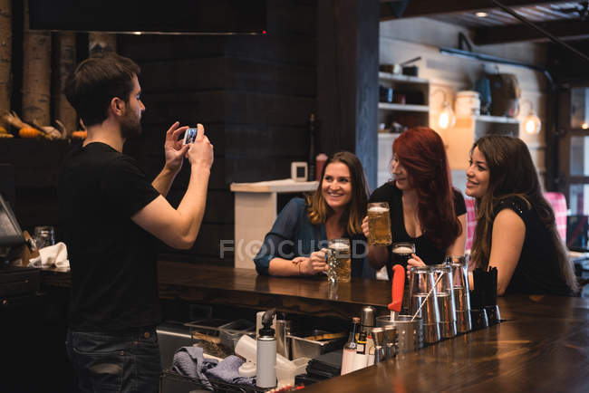 Bartender tirar fotos de mulheres no balcão de bar usando telefone celular — Fotografia de Stock