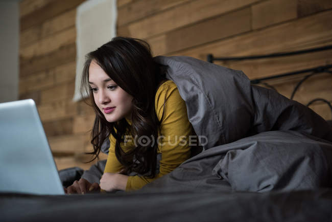 Mulher deitada na cama usando laptop no quarto em casa — Fotografia de Stock