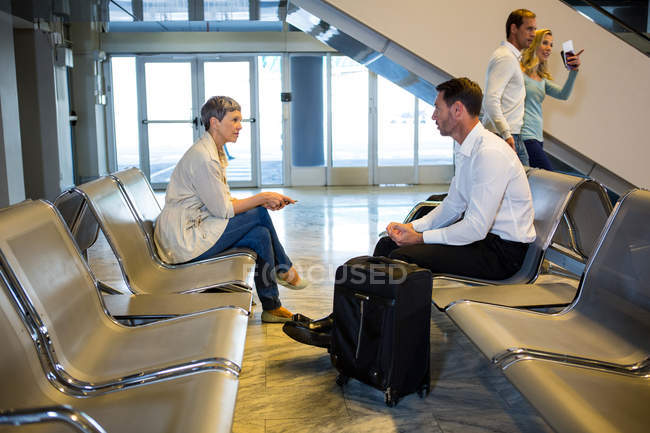 Pasajeros con maleta interactuando en la zona de espera en la terminal del aeropuerto - foto de stock