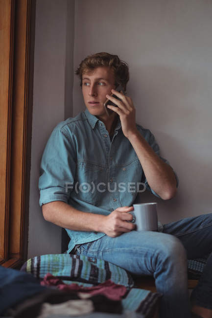 Мужчина держит кофейную чашку разговаривая по мобильному телефону дома — стоковое фото