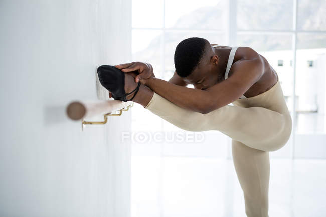 Ballerino che si allunga su una sbarra mentre pratica la danza classica in studio — Foto stock