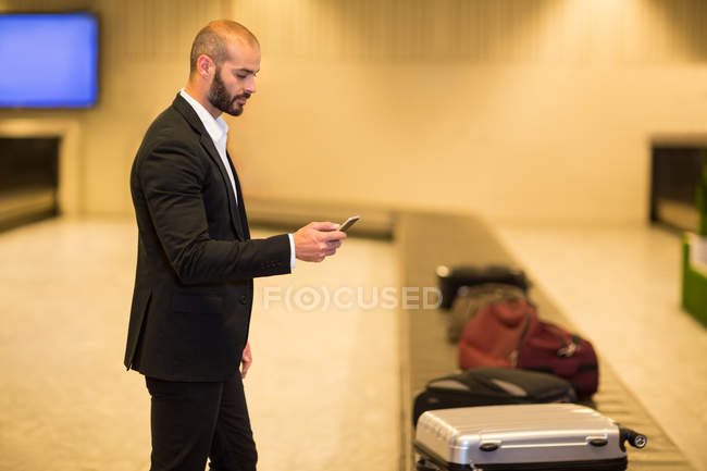 Businessman using mobile phone near baggage claim area at airport — Stock Photo
