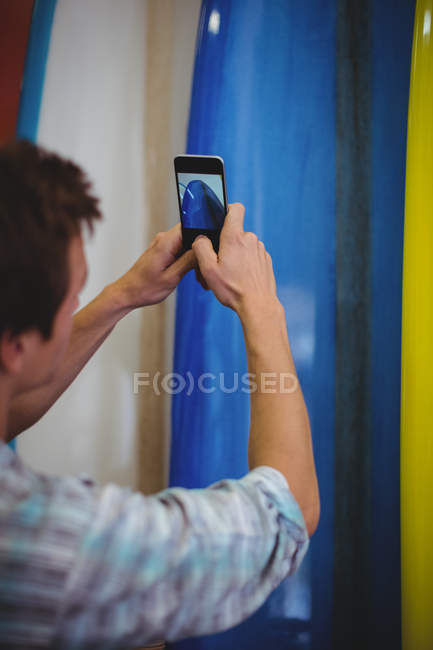 Visão traseira do homem tirando fotos de pranchas de surf no telefone celular na loja — Fotografia de Stock