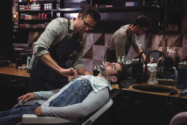 Man getting  beard shaved by hairdresser with razor in barber shop — Stock Photo
