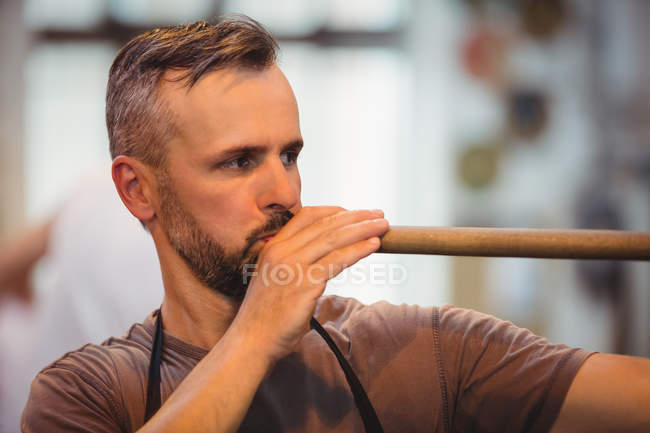 Стеклодув продувает трубу на стекольном заводе — стоковое фото